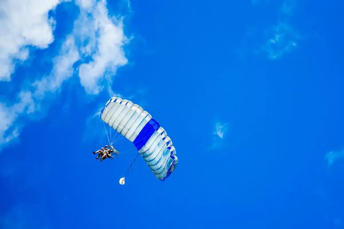 Pessoas realizando salto de paraquedas com céu azul ao fundo