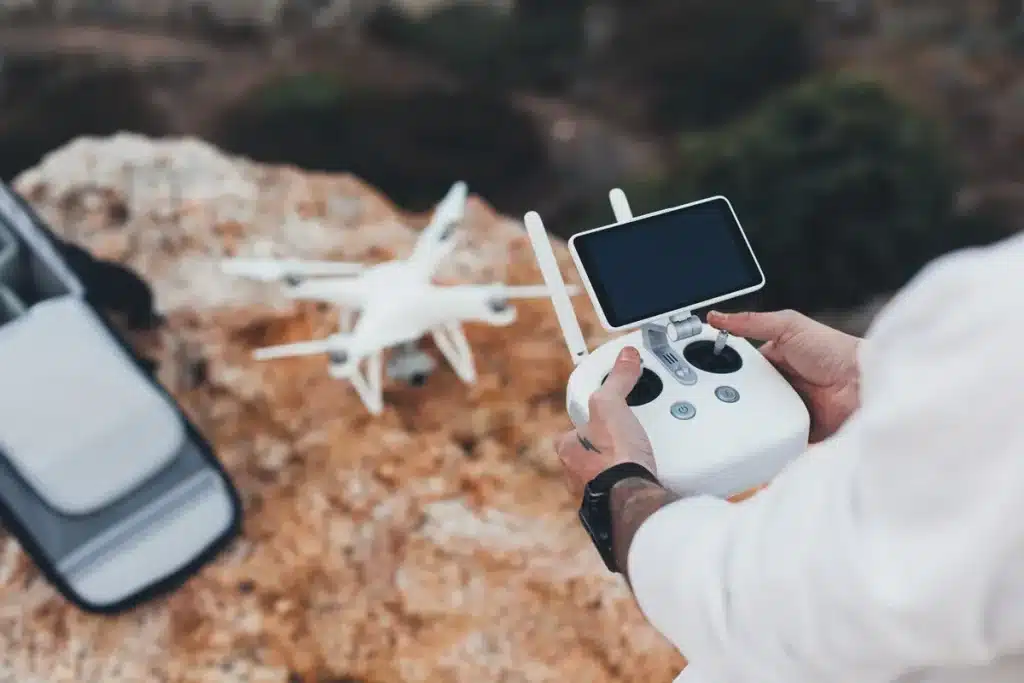 Pessoa operando um drone com controle remoto e tela integrada, em um ambiente externo rochoso.