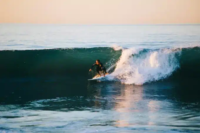 Surfista deslizando sobre uma onda no oceano, com a luz dourada do pôr do sol refletindo na água.